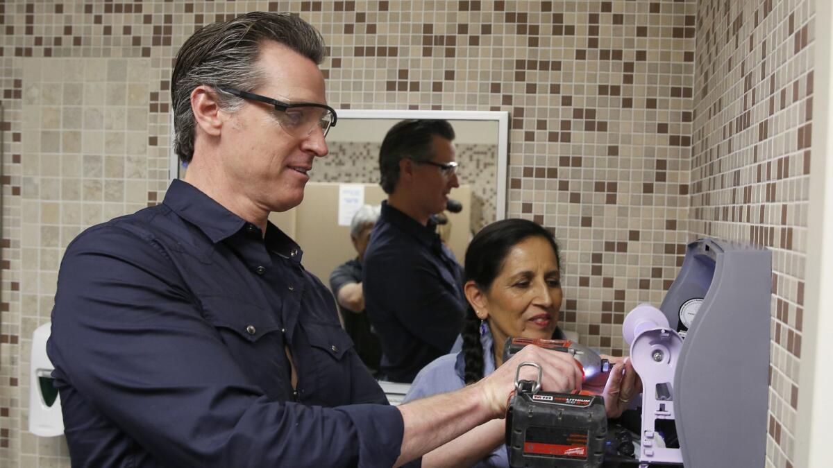 On International Workers' Day on Wednesday, Gov. Gavin Newsom helps custodian Maria Arambula replace towels in a restroom dispenser at American River College in Sacramento.