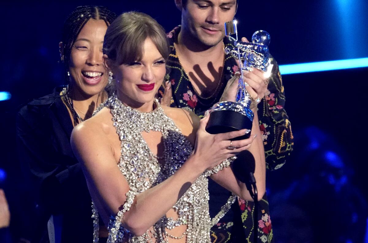 Taylor Swift holds up a moon person trophy at the MTV Video Music Awards with two people behind her