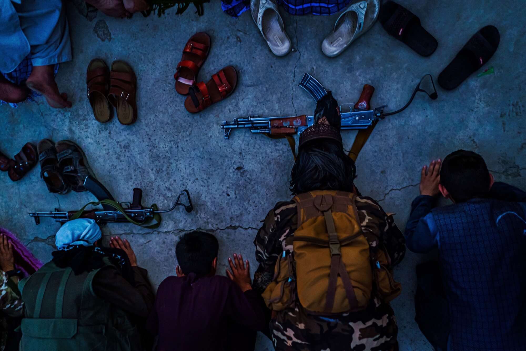 A top-down shot of men kneeling to pray with their sandals and rifles in front of them.
