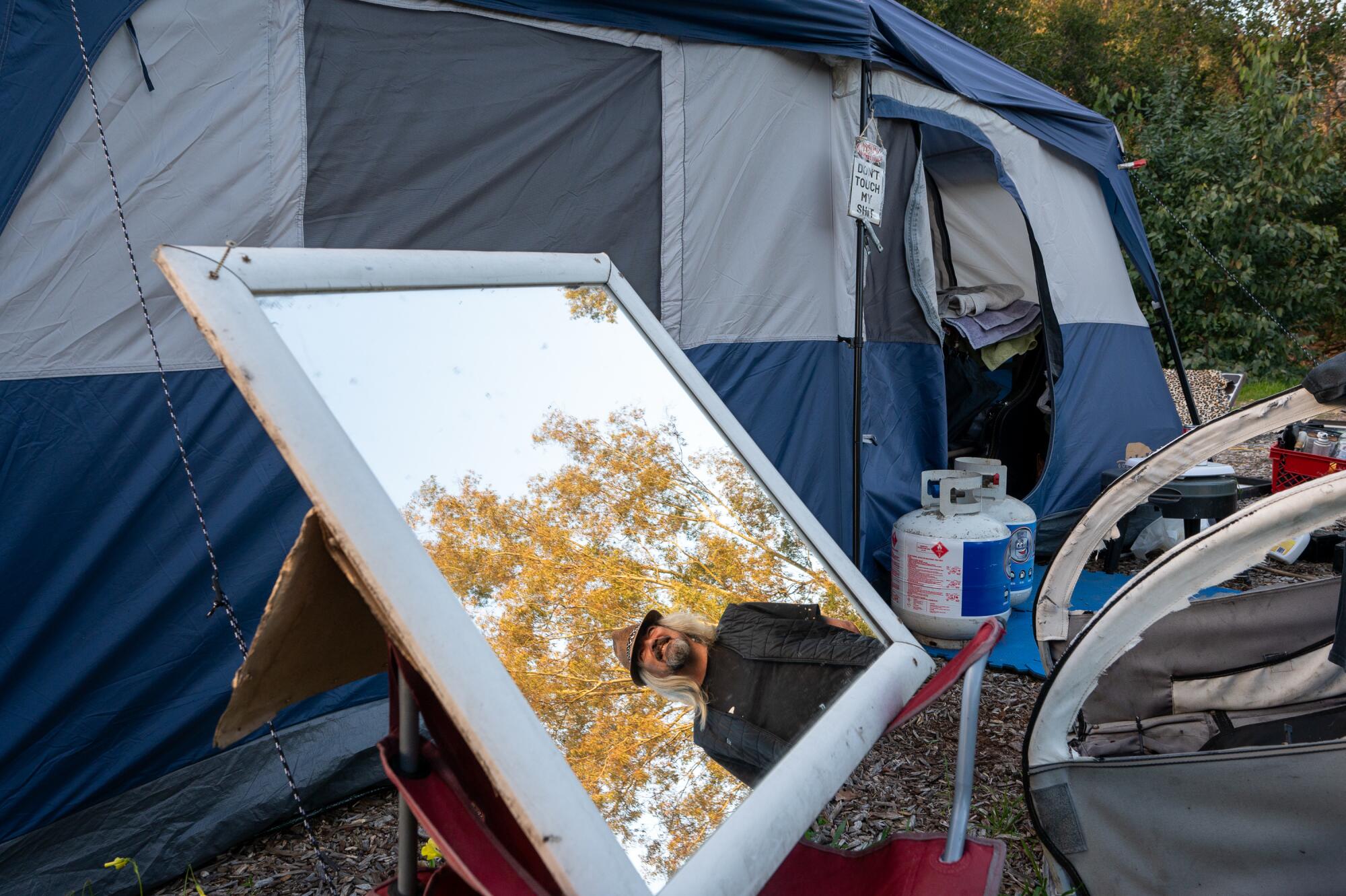 A man's image is reflected in a mirror at a homeless encampment.