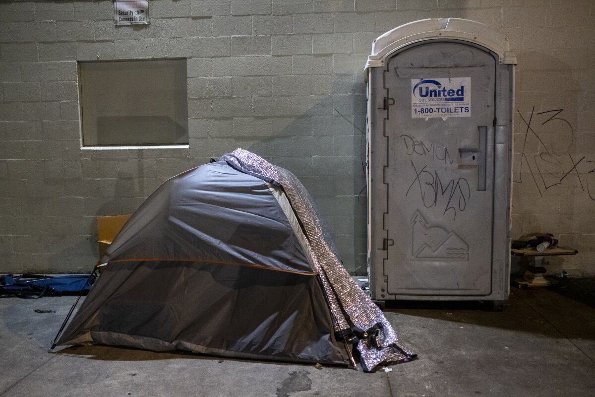 A tent next to a portable toilet on a sidewalk 