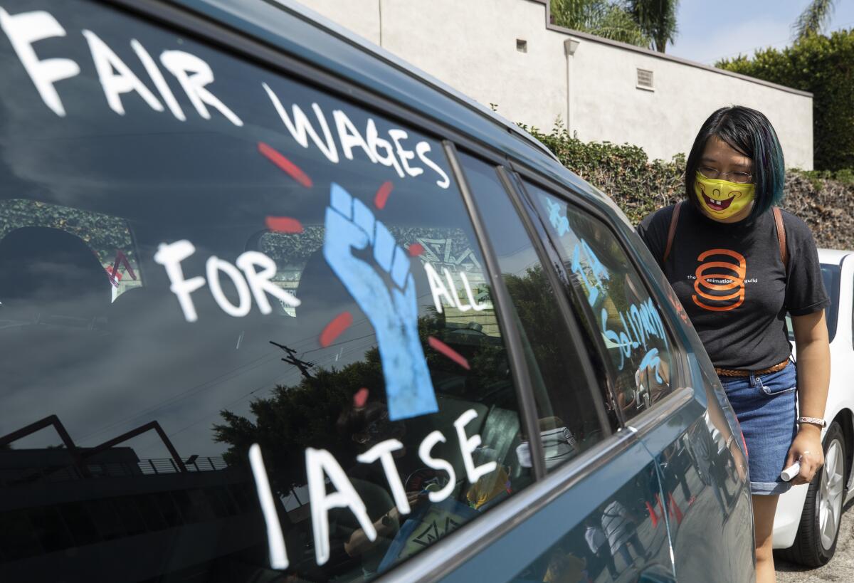 Crystal Kan, a storyboard artist, draws pro-labor signs on cars of union members during a rally.