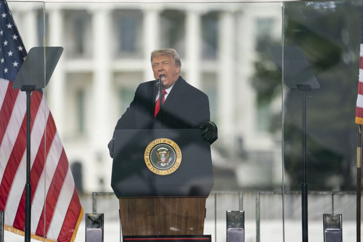 President Trump speaks at a lectern flanked by U.S. flags while behind bulletproof glass at a rally Wednesday in Washington.