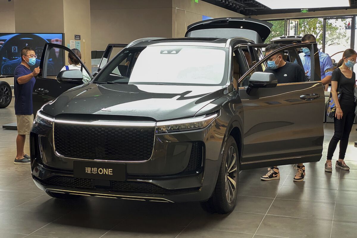 People wearing face masks to help curb the spread of the coronavirus look at a new Chinese-made electric Li One SUV at a dealership in Beijing on Aug. 2, 2020. China's sales of SUVs, minivans and sedans fell 6% last year compared with 2019 after demand plunged due to the coronavirus and rebounded in the second half. (AP Photo/Andy Wong)