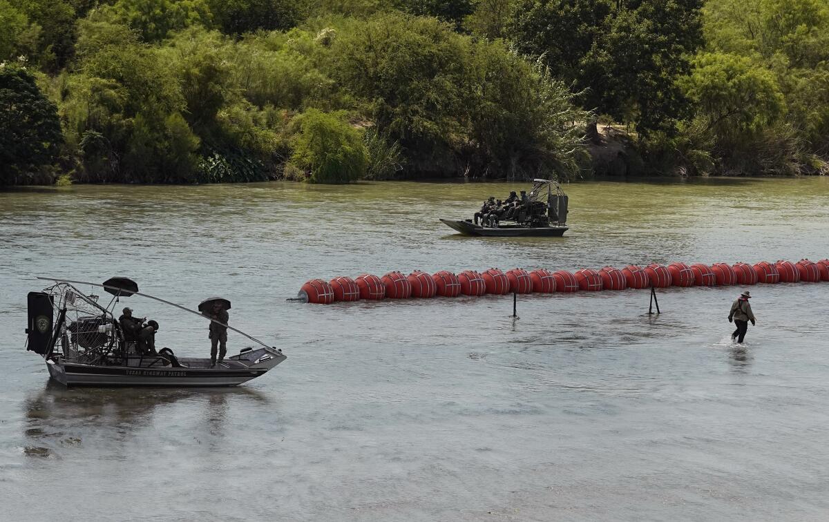 Texas State Troopers watch from an airboat as workers deploy a string of large buoys
