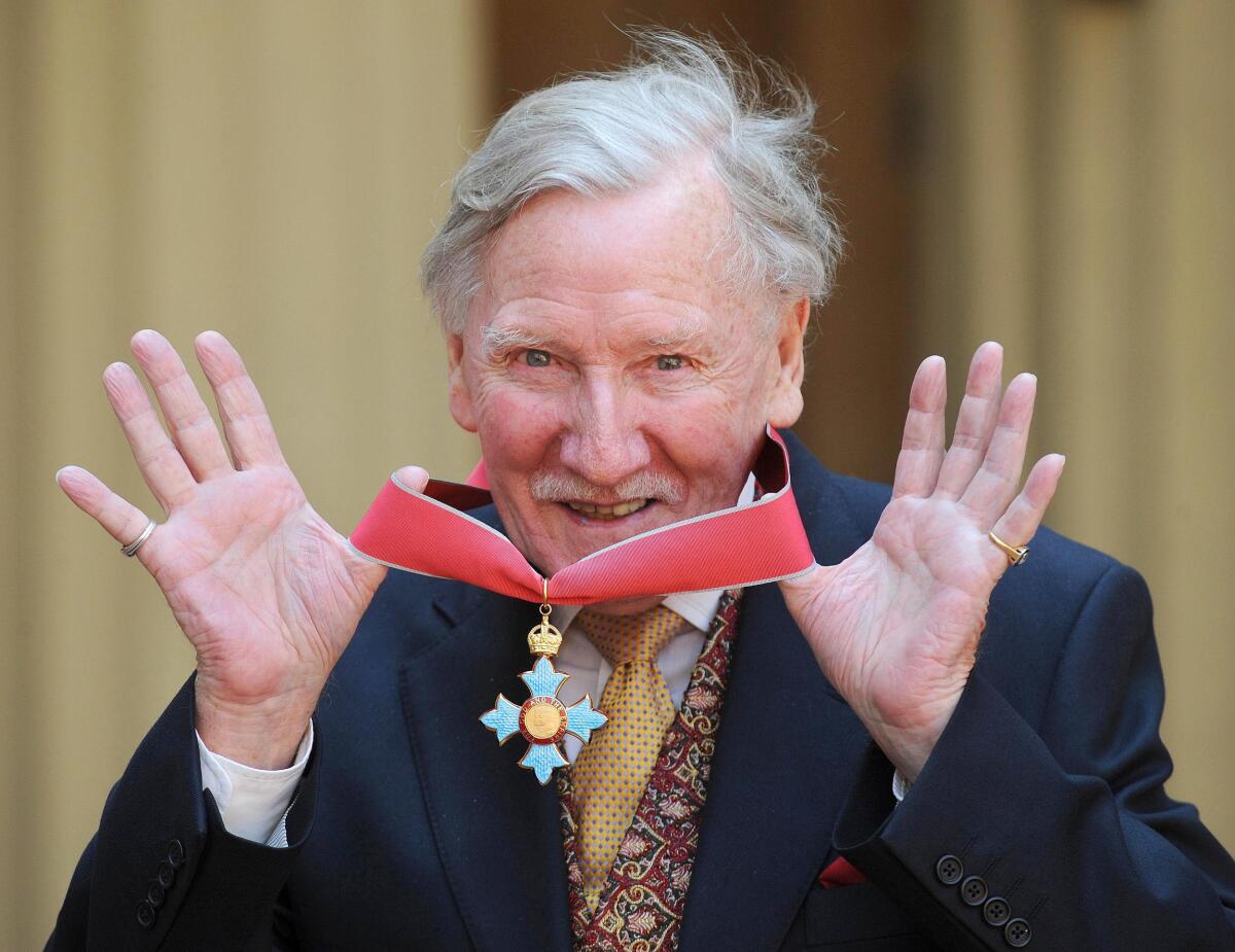 A man with gray hair smiling in a suit and holding a red ribbon with a medal around his neck