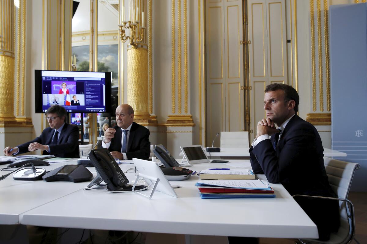 French President Emmanuel Macron, right, listens as he attends with French Foreign Minister Jean-Yves le Drian, center, an international video-conference on coronavirus vaccination at the Elysee Palace in Paris, on Monday.