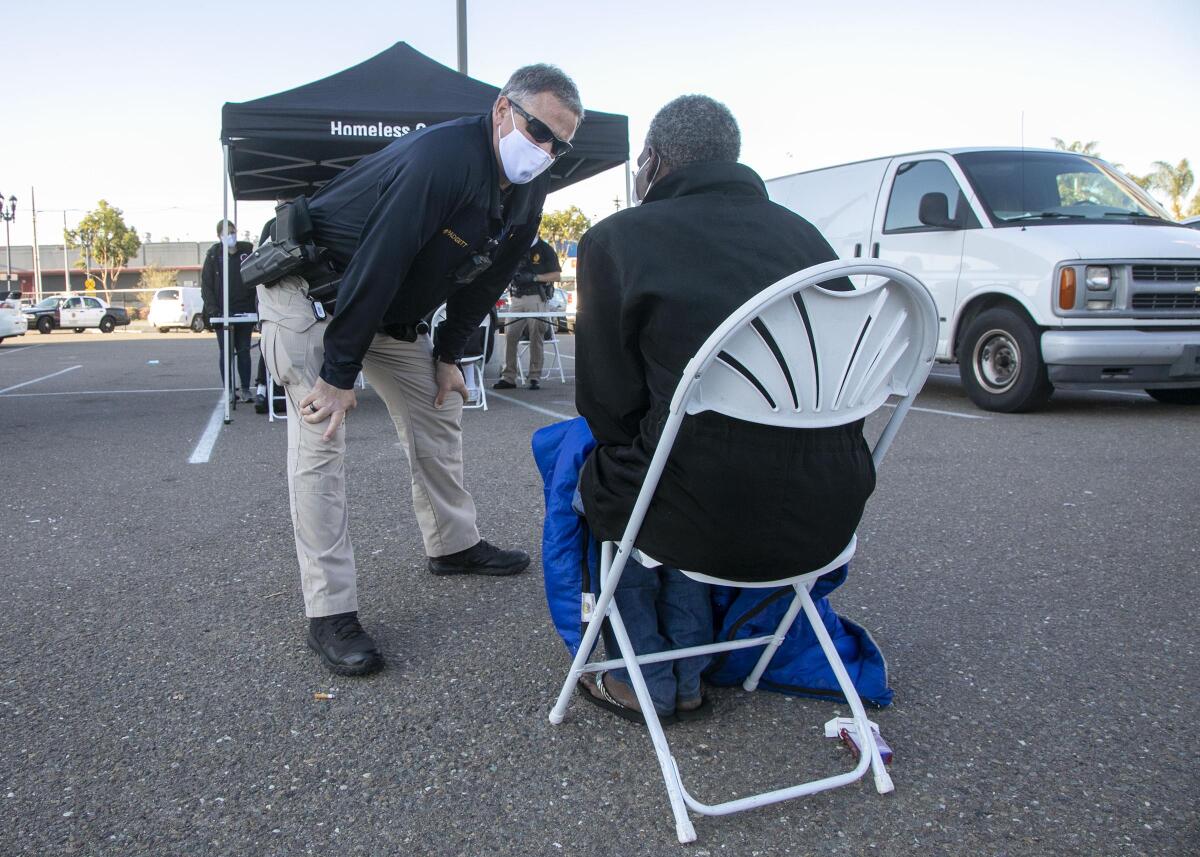 San Diego Police Homeless Outreach Team officer Michael Padgett talks to a homeless person going through the screening process in an East Village parking lot in downtown San Diego on Thursday. People living on the street are being offered shelter in the San Diego Convention Center during the COVID-19 pandemic.