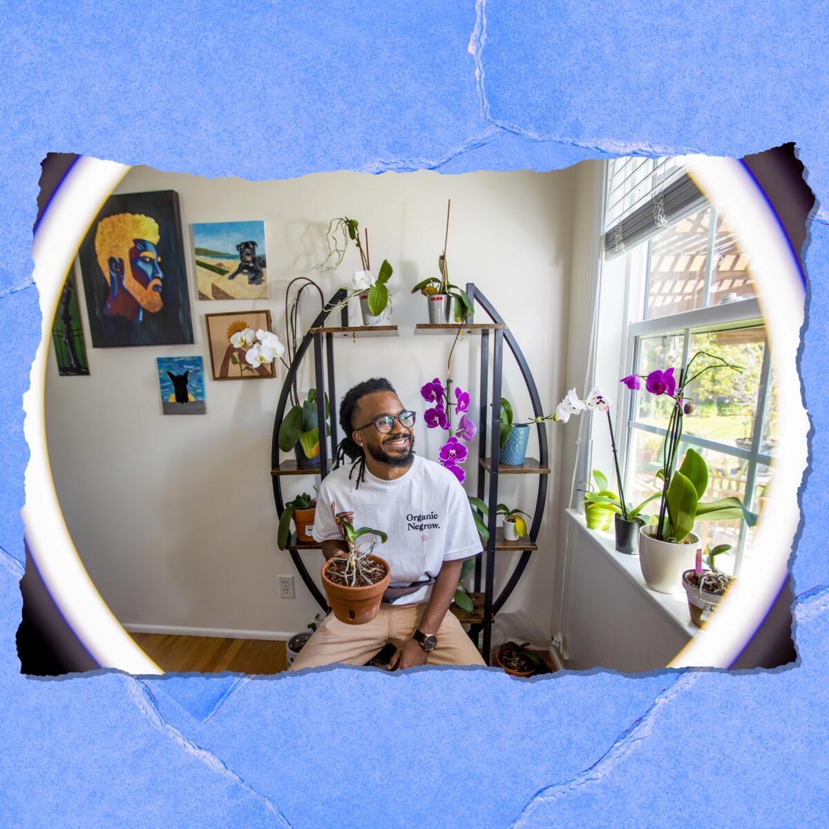 A smiling man sits inside a house next to an open window. Plants are on shelves around him.