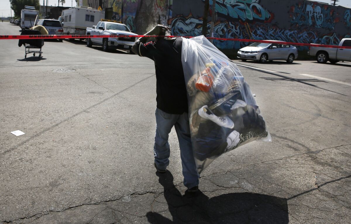 A homeless man leaves an encampment area with his belongings in a bag. (Christian K. Lee / Los Angeles Times)