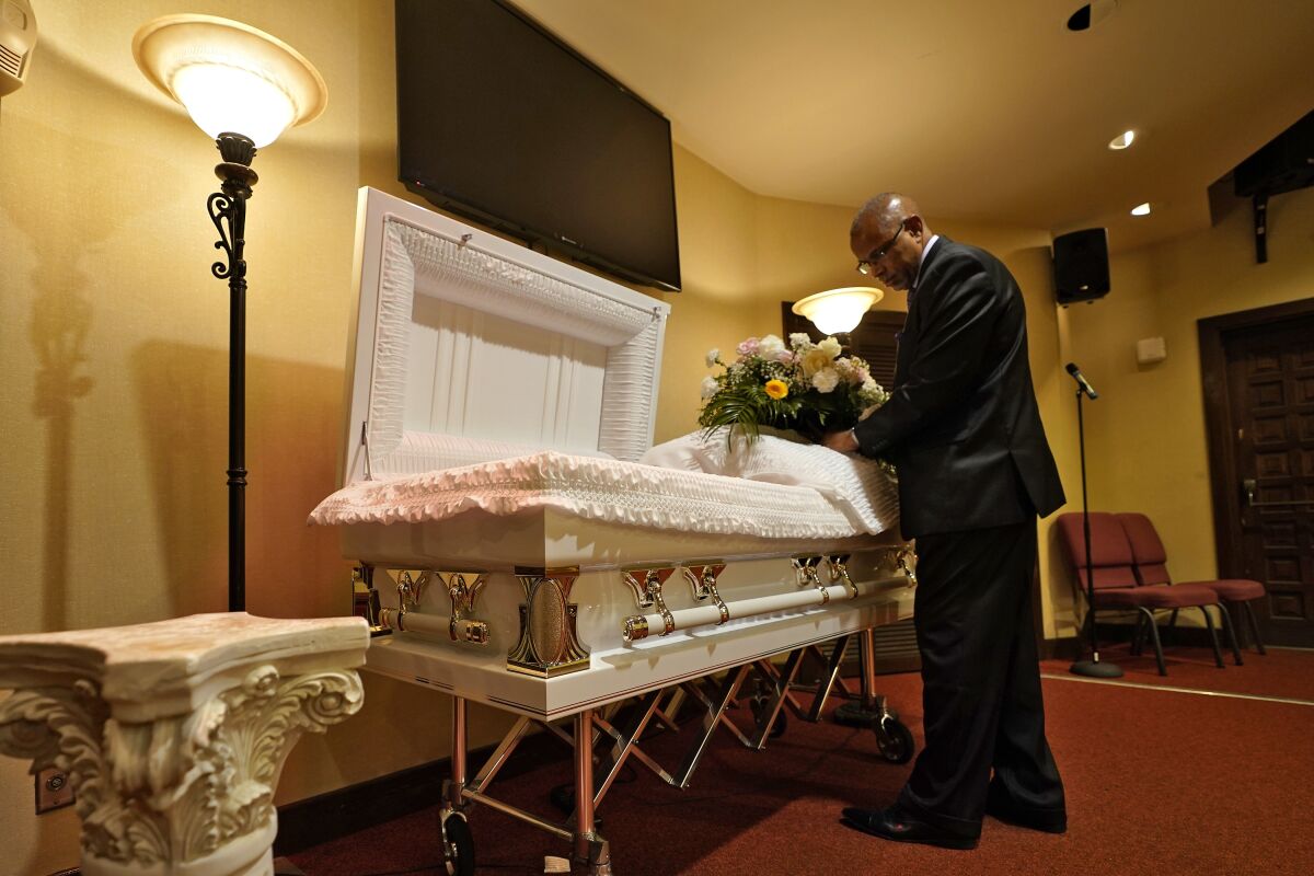 FILE - In this Thursday, Sept. 2, 2021 file photo, a funeral director arranges flowers on a casket before a service in Tampa, Fla. According to a study published Thursday, Oct. 7, 2021, by the medical journal Pediatrics, the number of U.S. children orphaned during the COVID-19 pandemic may be larger than previously estimated, and the toll has been far greater among Black and Hispanic Americans. (AP Photo/Chris O'Meara, File)