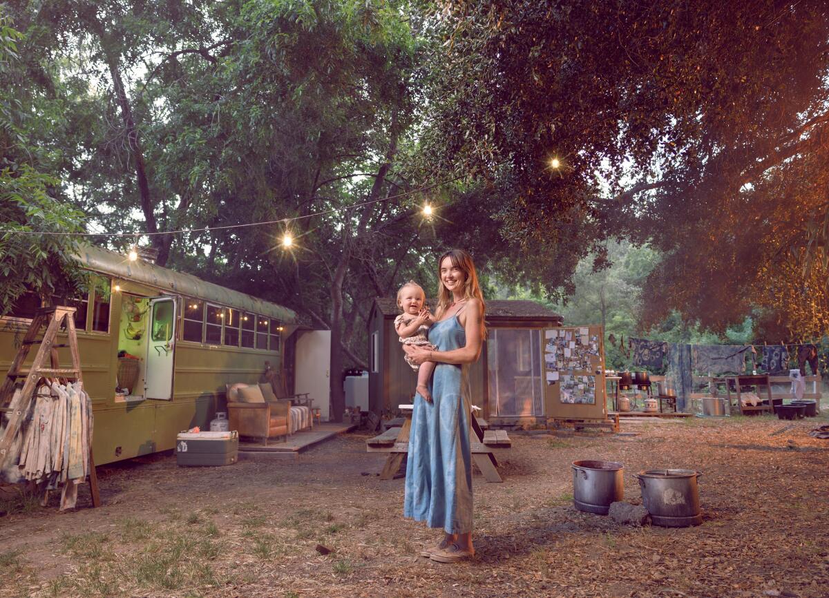 A photo of a mother holding her 16-month-old daughter near a bus that has been converted into a home.