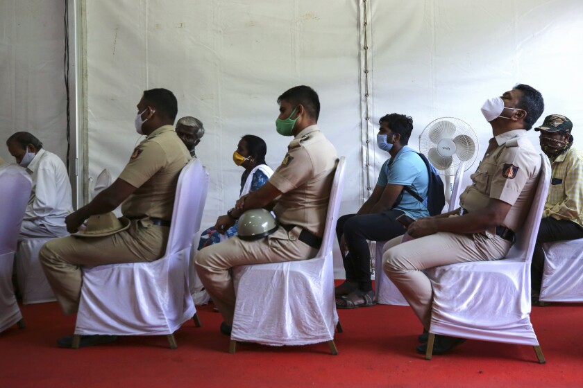 Indian policemen wait with others to receive the third dose of COVID-19 vaccine at a vaccination center in Bengaluru, India, Monday, Jan. 10, 2022. Healthcare and front-line workers along with people above age 60 with health problems lined up Monday at vaccination centers across India to receive a third vaccination as infections linked to the omicron variant surge. India calls these 'precautionary' doses and not boosters. (AP Photo/Aijaz Rahi)