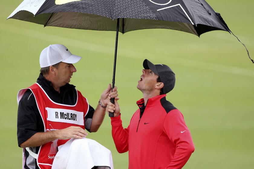 Rory McIlroy and caddie J.P. Fitzgerald seek shelter under an umbrella during the first round of the Australian Open on Thursday.