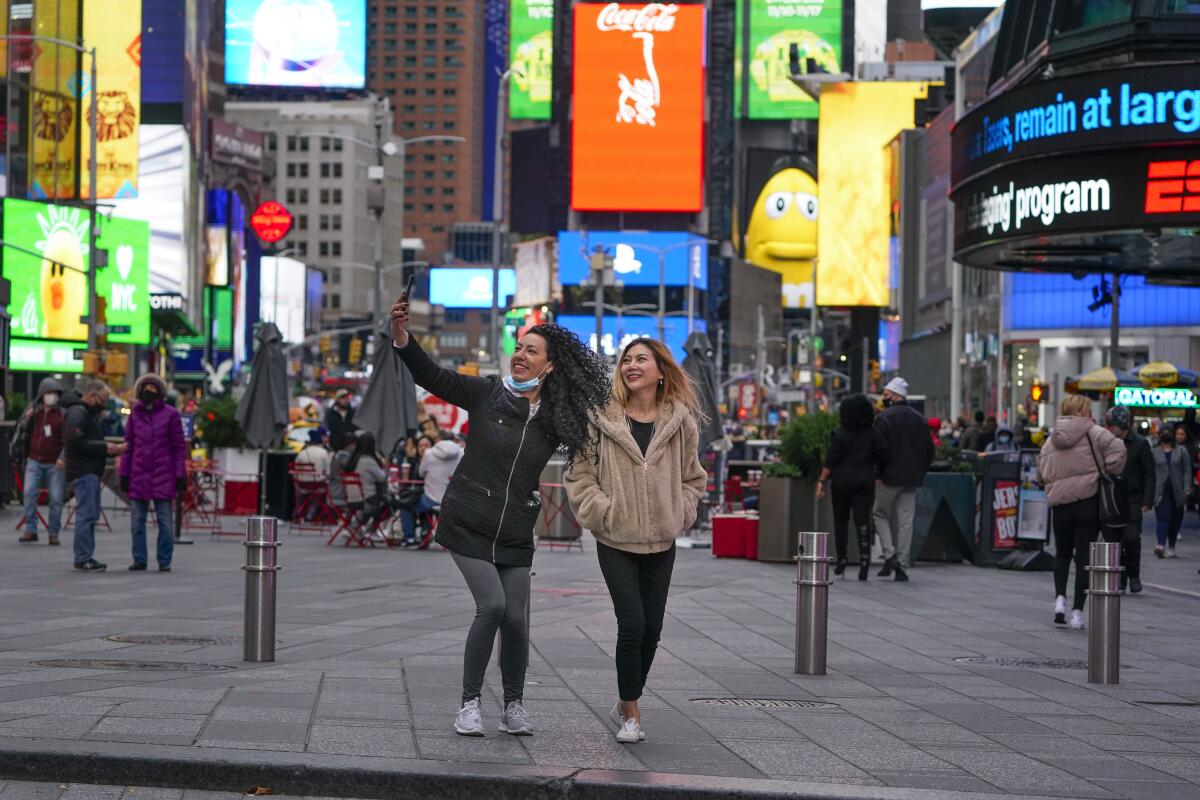 Two women pose for pictures in Times Square amide colorful jumbo screens and other people
