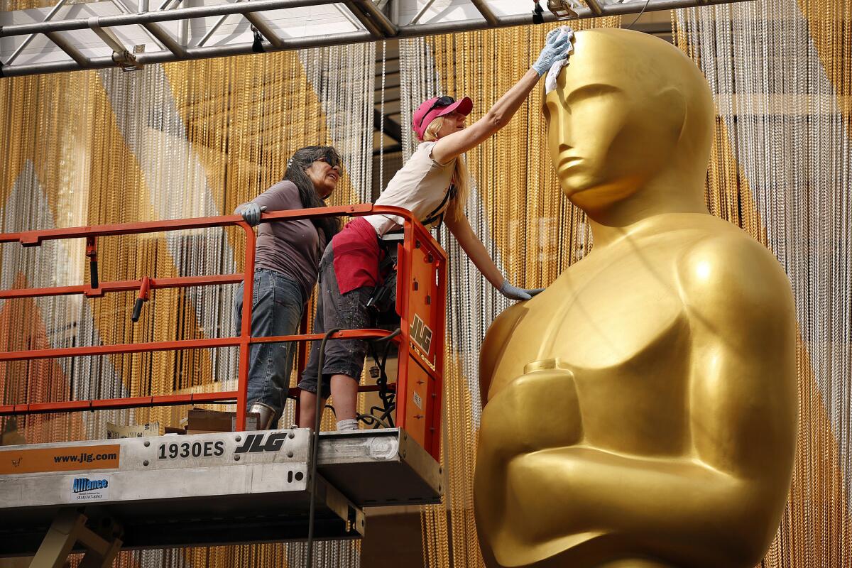 Scenic artist Dena D'Angelo, right, and Virginia Belloni, left, work to touch up a giant Oscar statue by the Academy Awards red carpet at the Dolby Theatre in Hollywood.