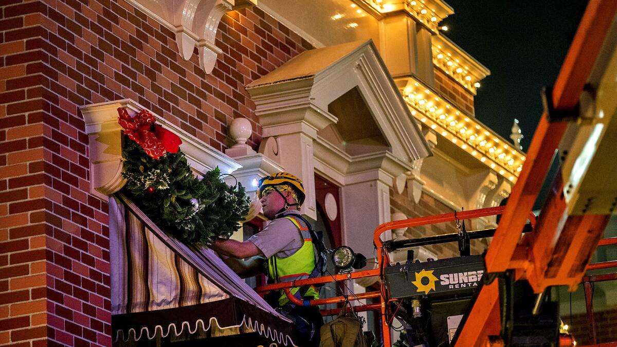 A worker fastens garland to a storefront awning overnight on Main Street U.S.A.