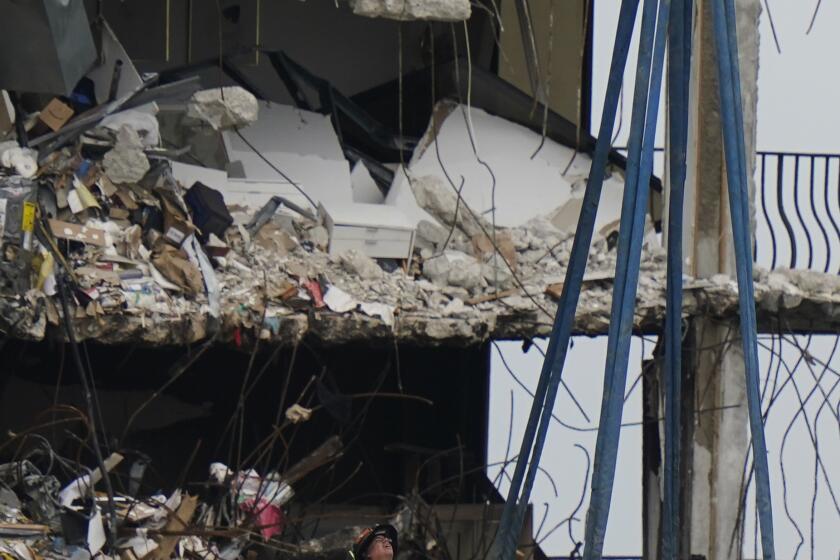 A crane prepares to remove a load of debris and household items, as search and rescue personnel work atop the rubble at the Champlain Towers South condo building where scores of people remain missing almost a week after it partially collapsed, Wednesday, June 30, 2021, in Surfside, Fla. (AP Photo/Lynne Sladky)