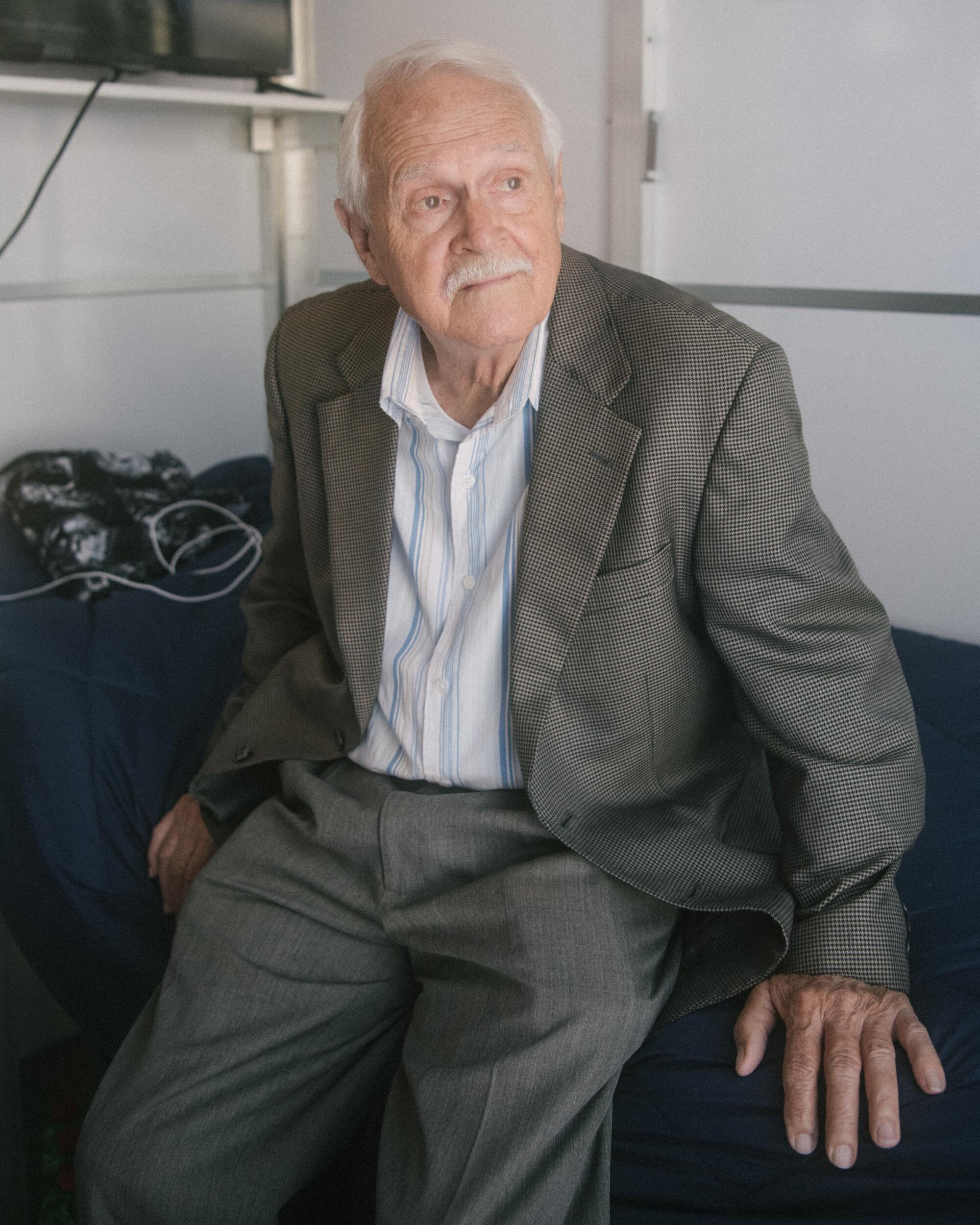 An elderly man poses in a suit. 
