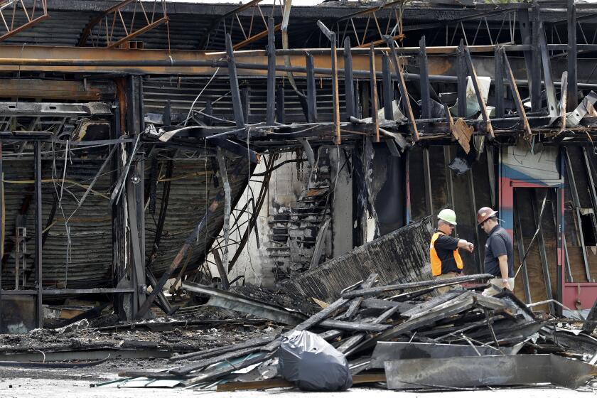 Dos trabajadores evalúan los daños causados a una tienda de artículos deportivos, el lunes 1 de junio de 2020, en Tampa, Florida, después de que el negocio fuera saqueado e incendiado durante una protesta el sábado por la noche. (AP Foto/Chris O'Meara)