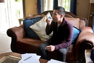  Javier Muniz, seated on a couch holds onto a thermometer in his mouth.