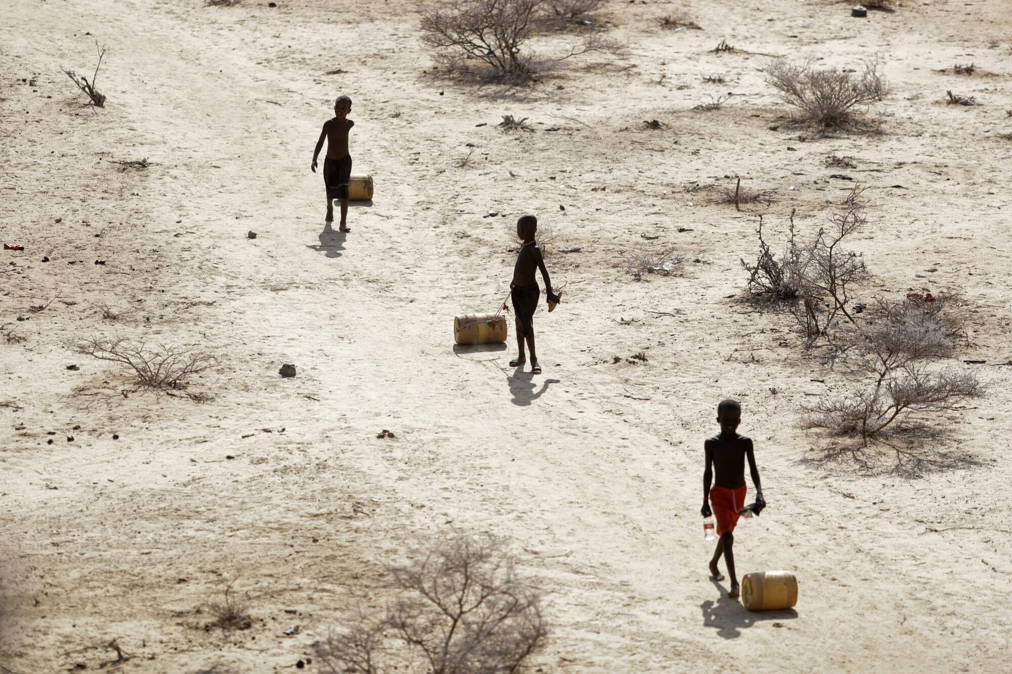 Boys pull containers filled with water along a dusty path.
