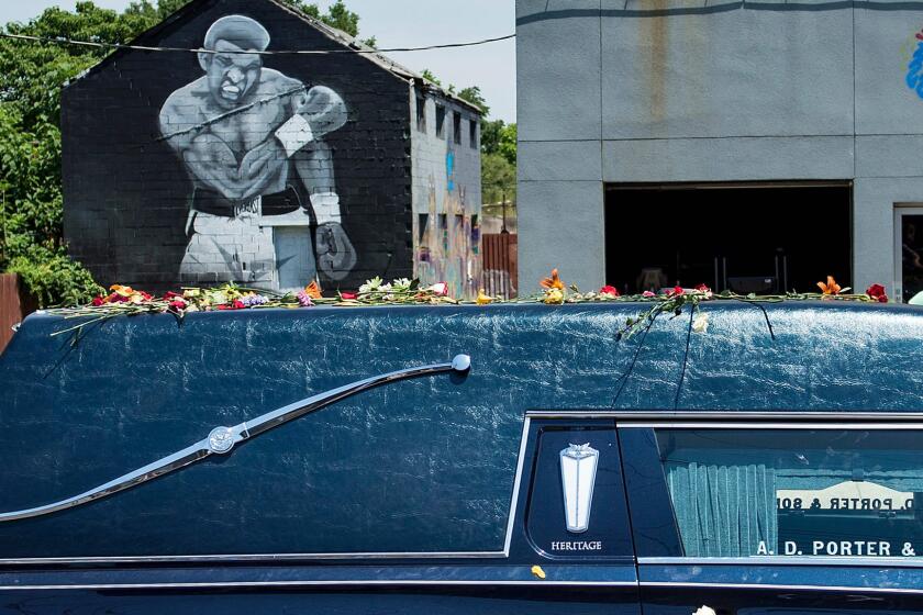 A hearse with the remains of boxing legend Muhammad Ali passes a mural depicting his 1965 victory over Sonny Liston on the way to Cave Hill Cemetery June 10, 2016, in Louisville, Ky.