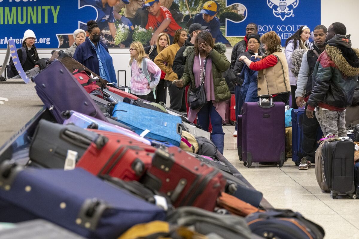 Travelers search through mountains of luggage at the baggage claim at Chicago Midway International Airport, Monday, Dec. 26, 2022, in Chicago. (Tyler Pasciak LaRiviere/Chicago Sun-Times via AP)