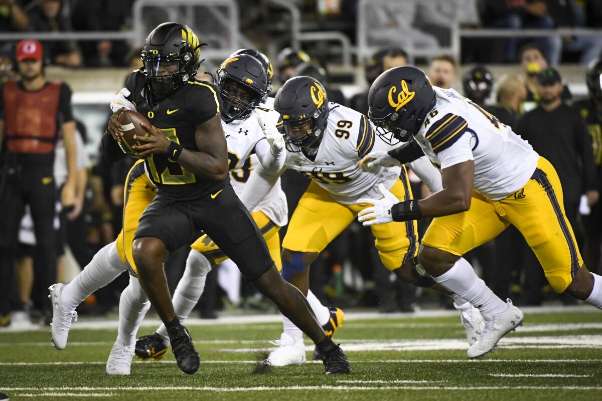 Oregon quarterback Anthony Brown (13) is pursued by California defensive end Ethan Saunders (99) and linebacker Marqez Bimage (46) during the second quarter of an NCAA college football game Friday, Oct. 15, 2021, in Eugene, Ore. (AP Photo/Andy Nelson)
