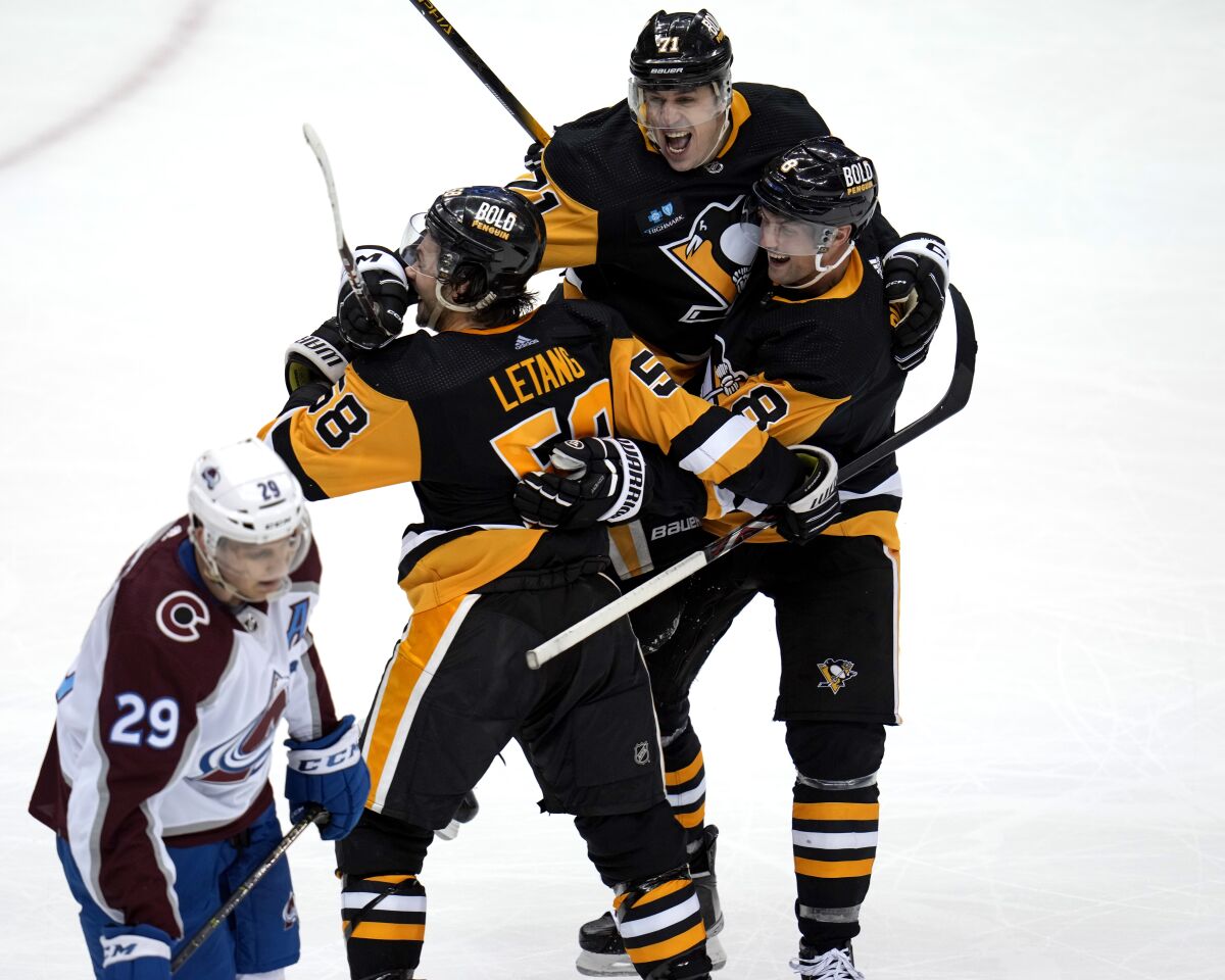 Pittsburgh Penguins' Kris Letang (58) celebrates his overtime goal with Evgeni Malkin (71) and Brian Dumoulin (8) as Colorado Avalanche's Nathan MacKinnon (29) skates off the ice, in an NHL hockey game in Pittsburgh, Tuesday, Feb. 7, 2023. (AP Photo/Gene J. Puskar)