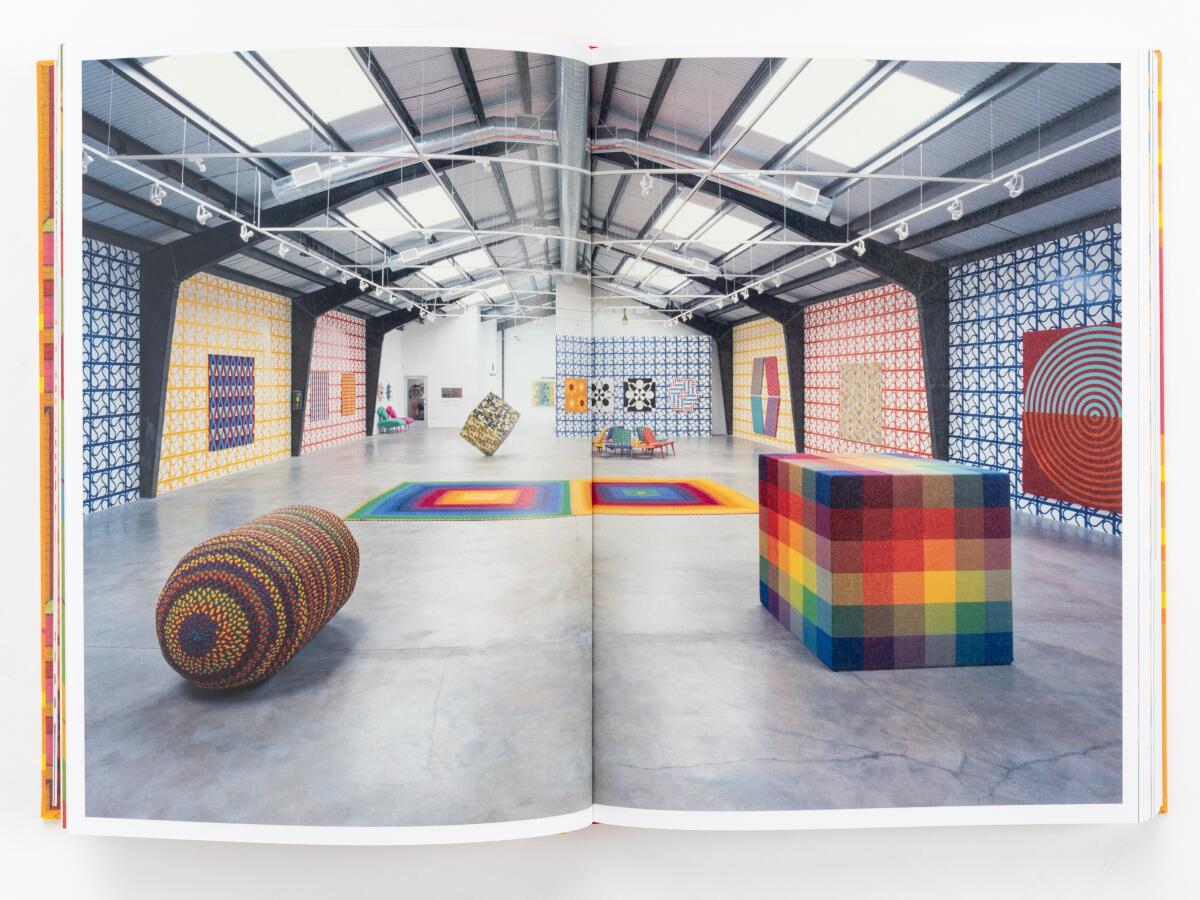 A book spread open shows two pages of colorful art, including rugs, furniture, wallpaper, paintings and a cube.