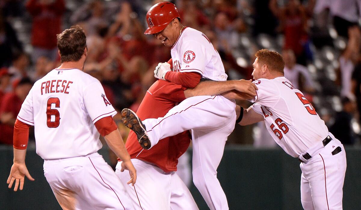 Angels pinch-hitter Efren Navarro leaps into the arms of a teammate after delivering a game-winning RBI single against the Mariners in the 16th inning late Friday night in Anaheim.