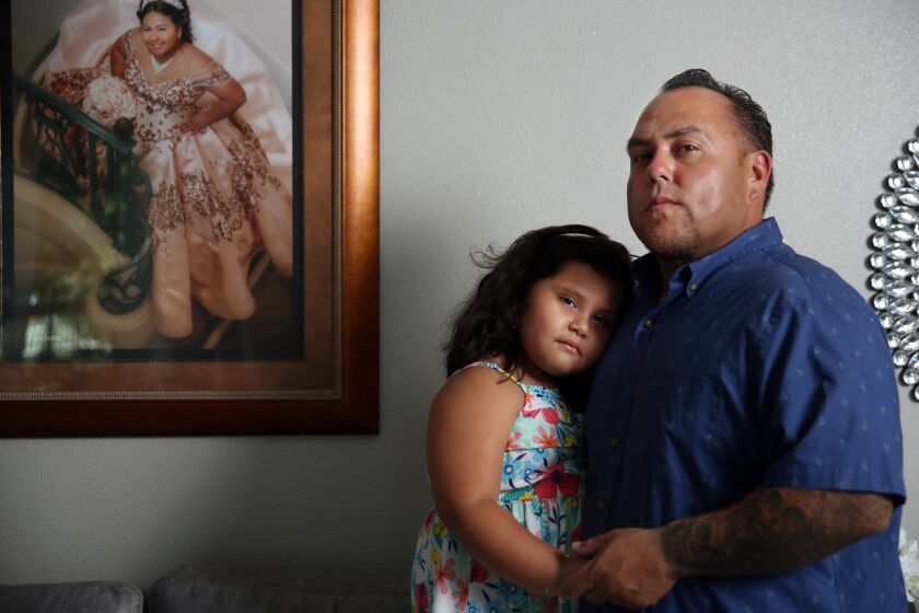 LOS ANGELES, CA - JULY 14: Rafael Saaverdra poses for a portrait with his daughter Gianna, 5, and a framed picture of his oldest daughter Gizzelle, 16, hangs beside them in Alhambra on Tuesday, July 14, 2020 in Los Angeles, CA. Saaverdra handles shipping containers from overseas and says that his worst fear is infecting his two daughters with the COVID-19. (Dania Maxwell / Los Angeles Times)
