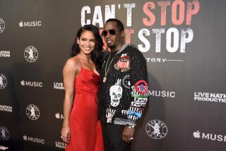 Cassie in a red sleeveless gown posing next to Sean "Diddy" Combs in a black jacket and sunglasses at a red carpet event