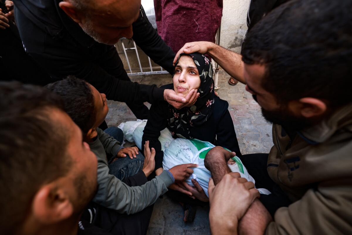 People try to comfort a woman holding the body of her baby girl killed in an Israeli strike in Rafah