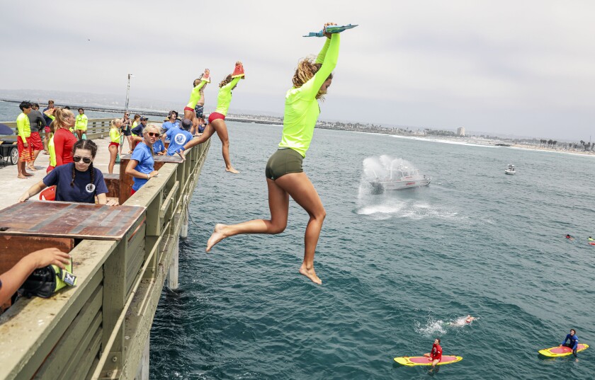 Members of the San Diego Junior Lifeguard program leap off the Ocean Beach Pier.