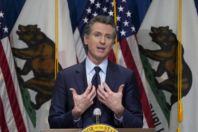 Governor Gavin Newsom gestures with both hands while speaking at a lectern in front of U.S. and California flags