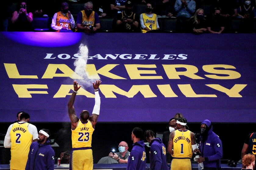 Three basketball players walk near a banner that says "Los Angeles Lakers Family." 