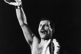 Freddie Mercury holding crown up to the sky, with royal cloak draped on other side of body