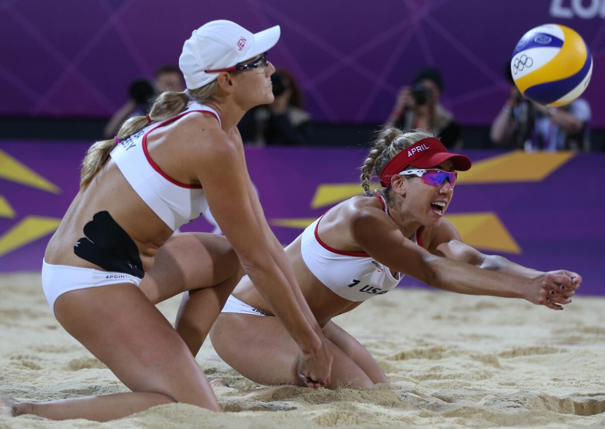 Jennifer Kessy and April Ross on their knees in the sand as they try to reach the volleyball.