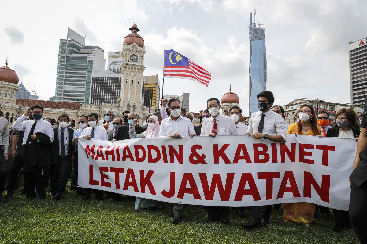 Malaysian opposition members Anwar Ibrahim, fourth from left, and Mahathir Mohamad, second from left in blue mask, hold a banner reading "Muhyiddin and Cabinet resign" during a protest in Kuala Lumpur, Malaysia, Monday, Aug. 2, 2021. Malaysian opposition lawmakers marched toward the parliament building in Kuala Lumpur to demand Prime Minister Muhyiddin Yassin to resign. (AP Photo/FL Wong)