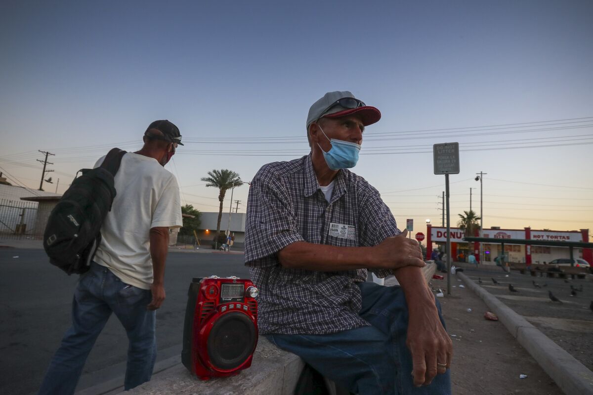 A 65-year-old man in a mask sits and waits for a day labor job in Calexico.