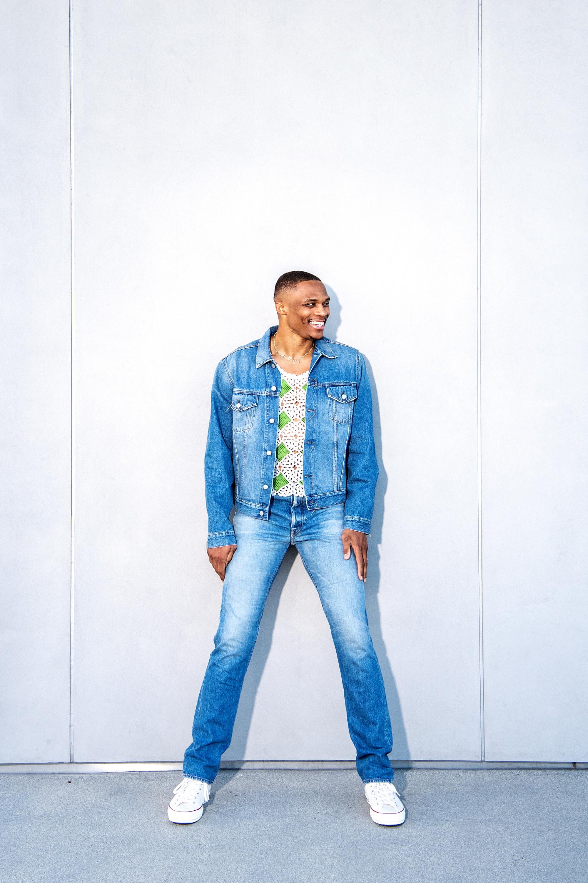 A man in denim jacket and jeans stands against a white background 