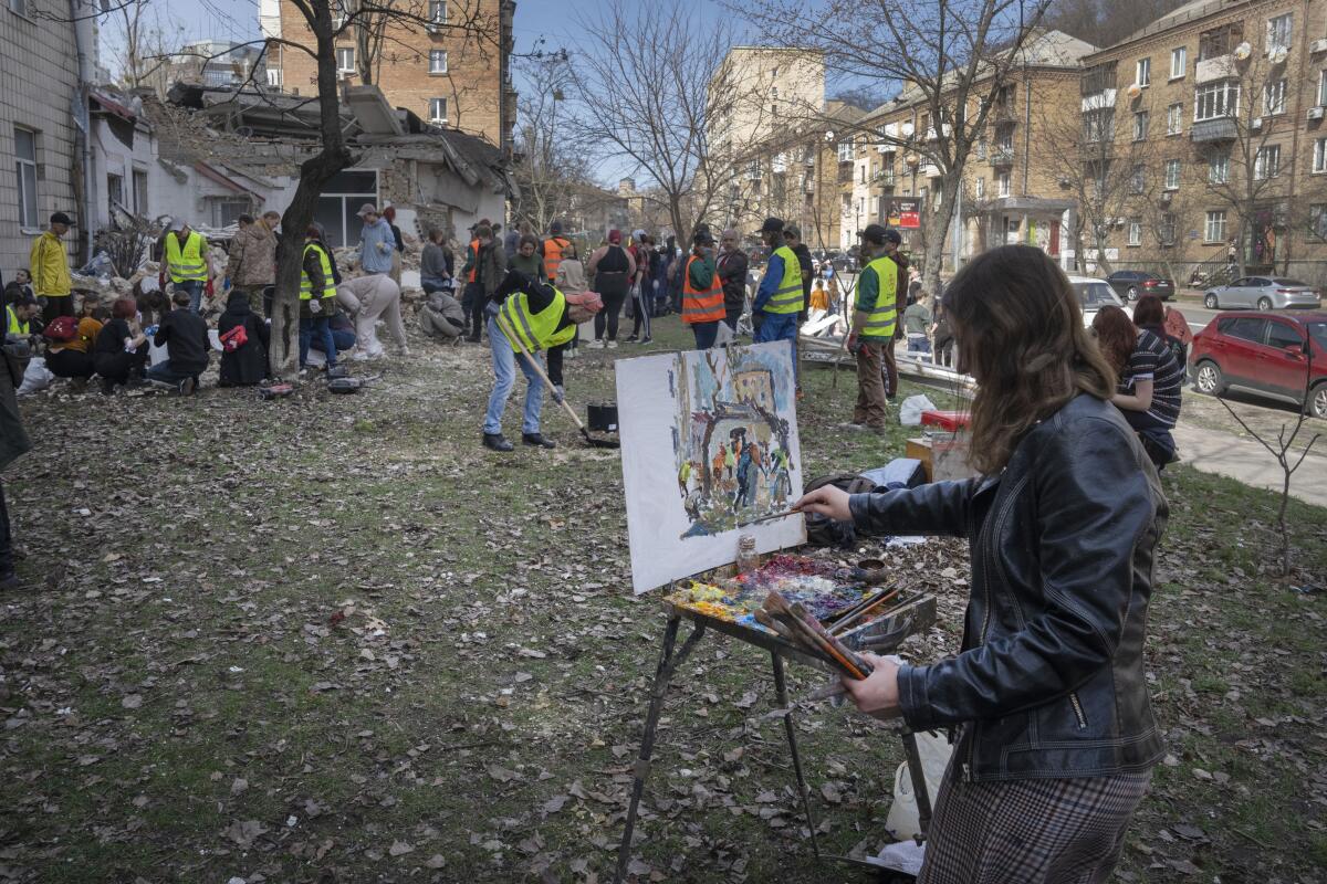 A student of Kyiv State Arts Academy paints as others clear rubble after a Russian missile attack.