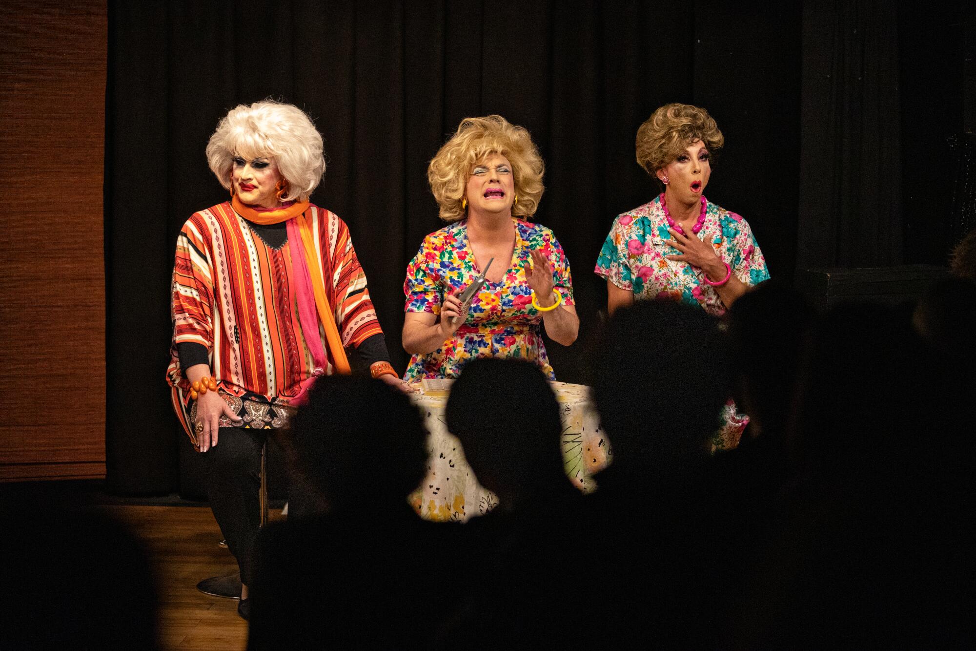 Three drag queens perform on a stage.