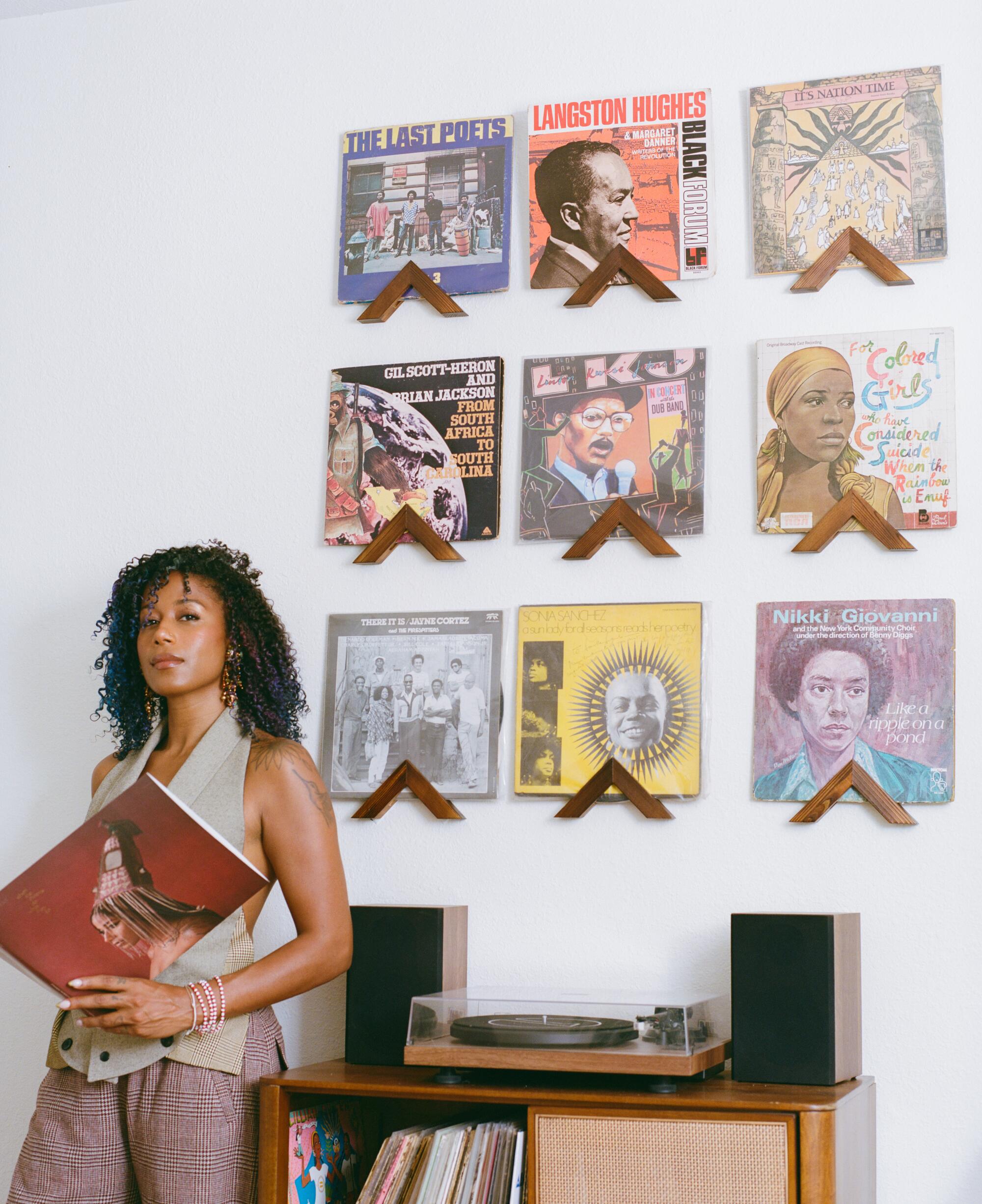 A woman stands in front of a wall displaying record album covers hanging over a record player
