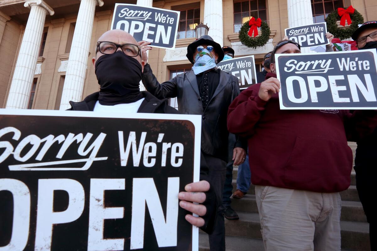 Protesters in masks hold signs that say Sorry We're Open on the steps of Stockton City Hall
