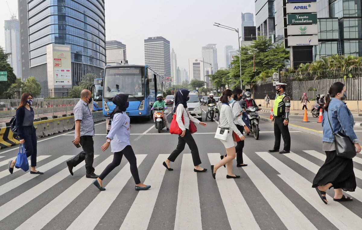 People, wearing a face mask as a precaution against the new coronavirus outbreak, walk on a pedestrian crossing at the main business district in Jakarta, Indonesia, Monday, Sept. 14, 2020. Indonesia's capital on Monday begins to reimpose large-scale social restrictions to control a rapid expansion in the virus cases. (AP Photo/Tatan Syuflana)