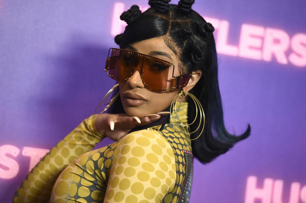 Cardi B wears large, square sunglasses and long nails and looks over her shoulder