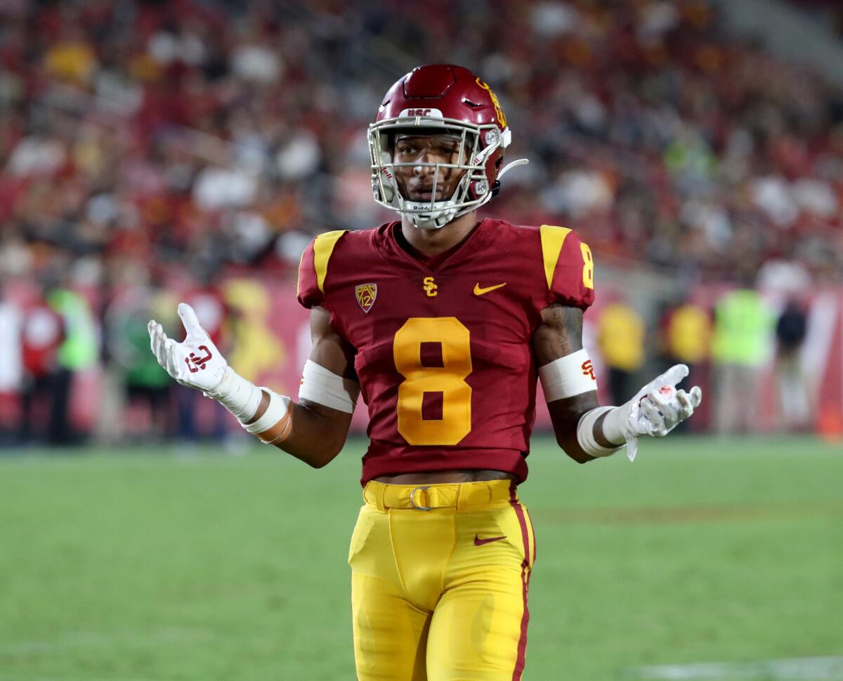 Chris Steele, in uniform, holds out both hands as he walks on the football field.